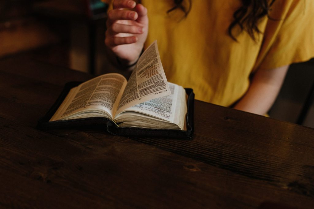 person reading Bible on top of brown wooden table